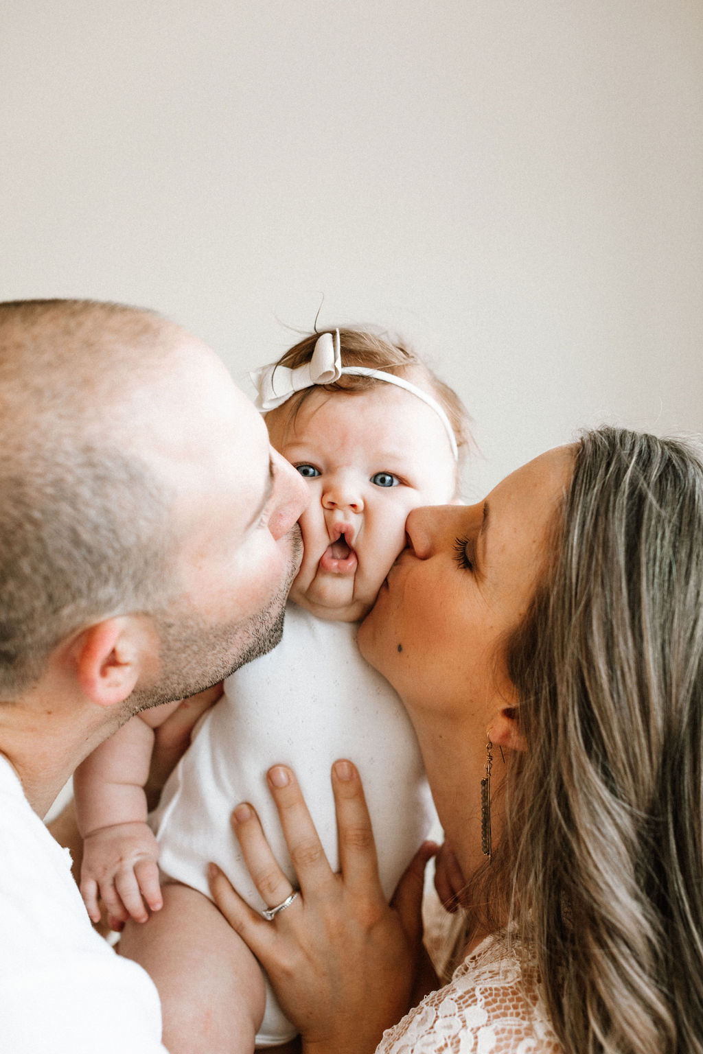 A mother and father each kissing their baby girl on the cheek